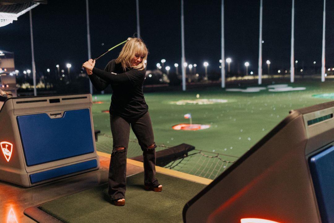 A woman is swinging a golf club on a golf course at night.
