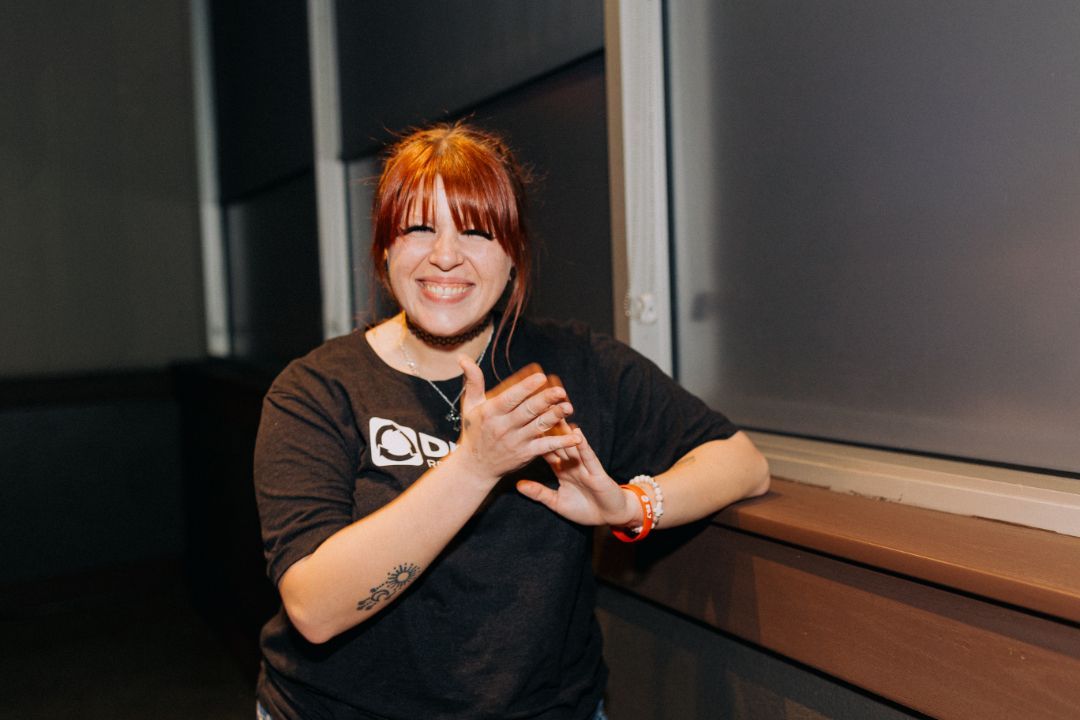 A woman with red hair is standing next to a window and clapping her hands.