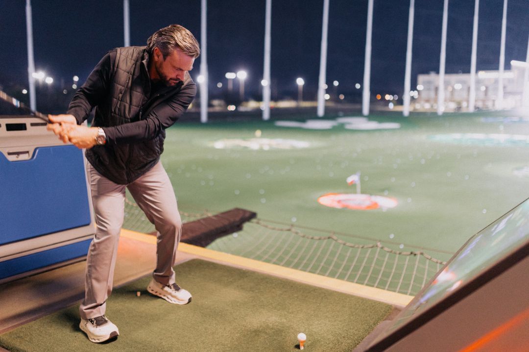 A man is swinging a golf club on a golf course at night.