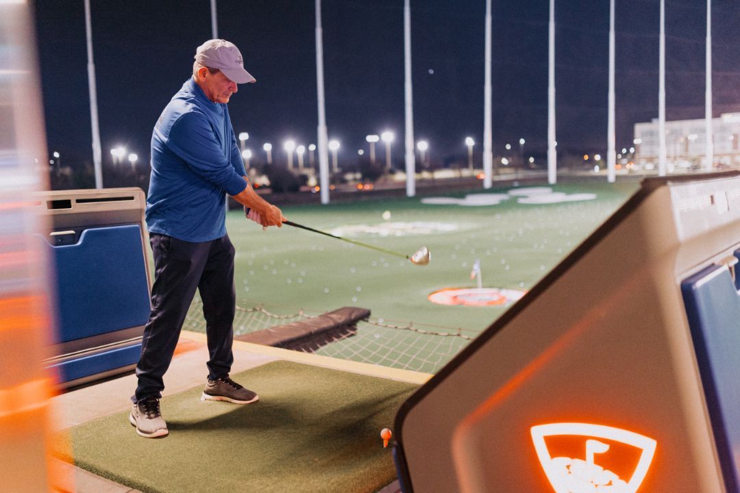 A man is swinging a golf club on a golf course at night.