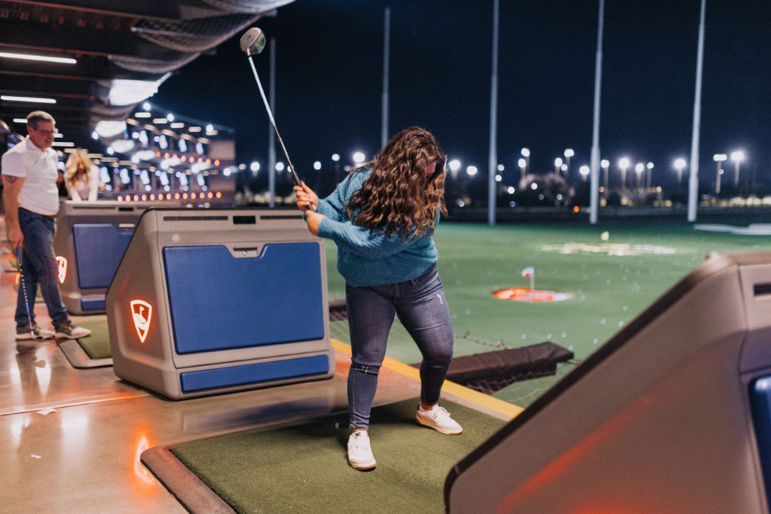 A woman is swinging a golf club on a golf course at night.