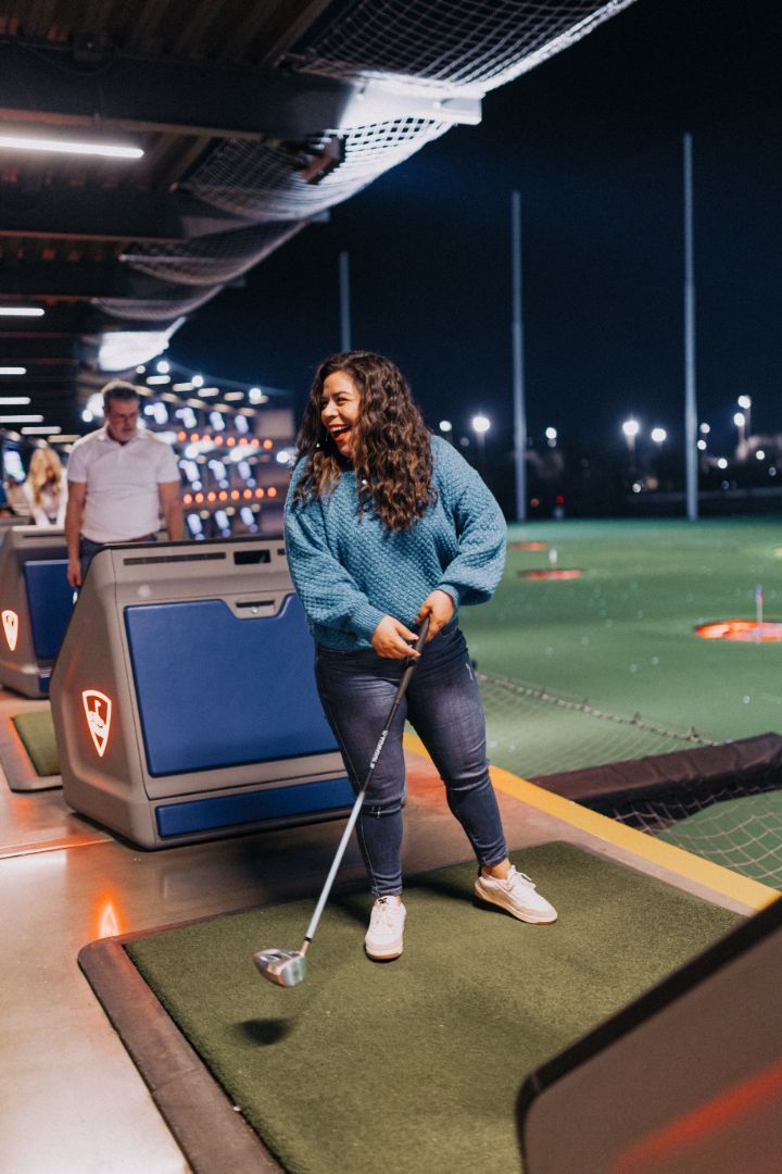A woman is swinging a golf club on a golf course at night.