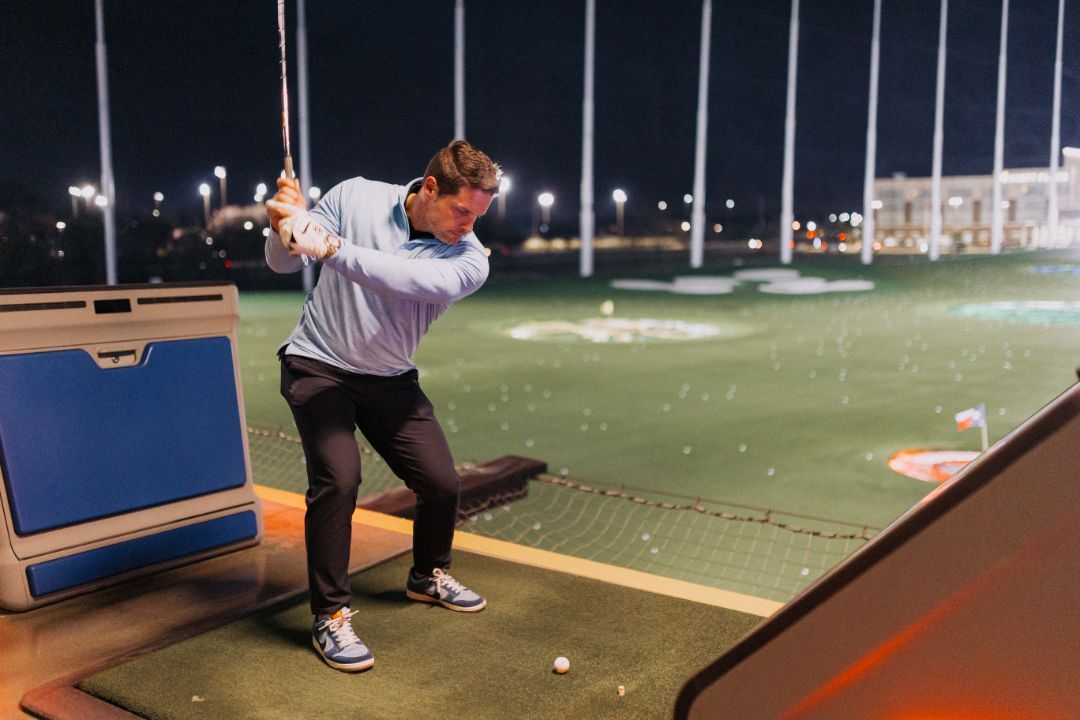 A man is swinging a golf club on a golf course at night.