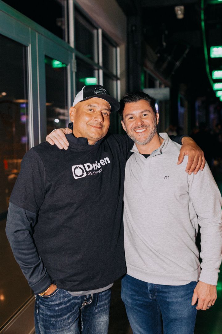 Two men are posing for a picture together in front of a window.