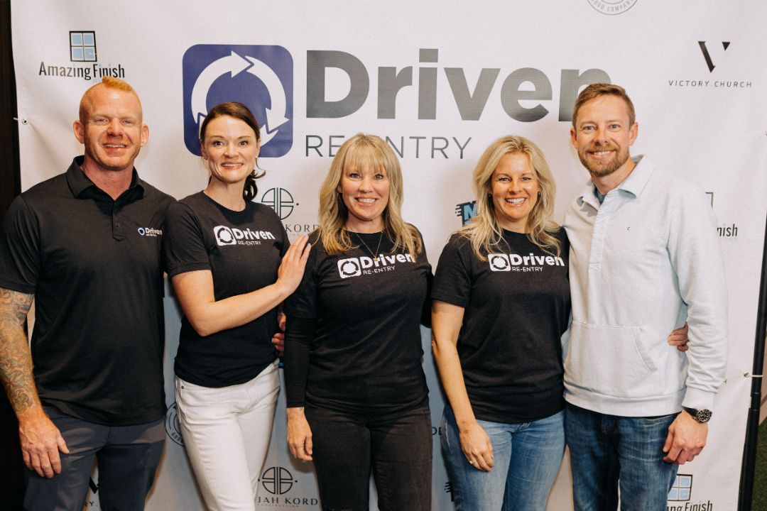 A group of people are posing for a picture in front of a banner that says driver recovery.