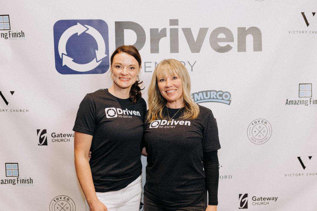 Two women are posing for a picture in front of a sign that says driven energy.