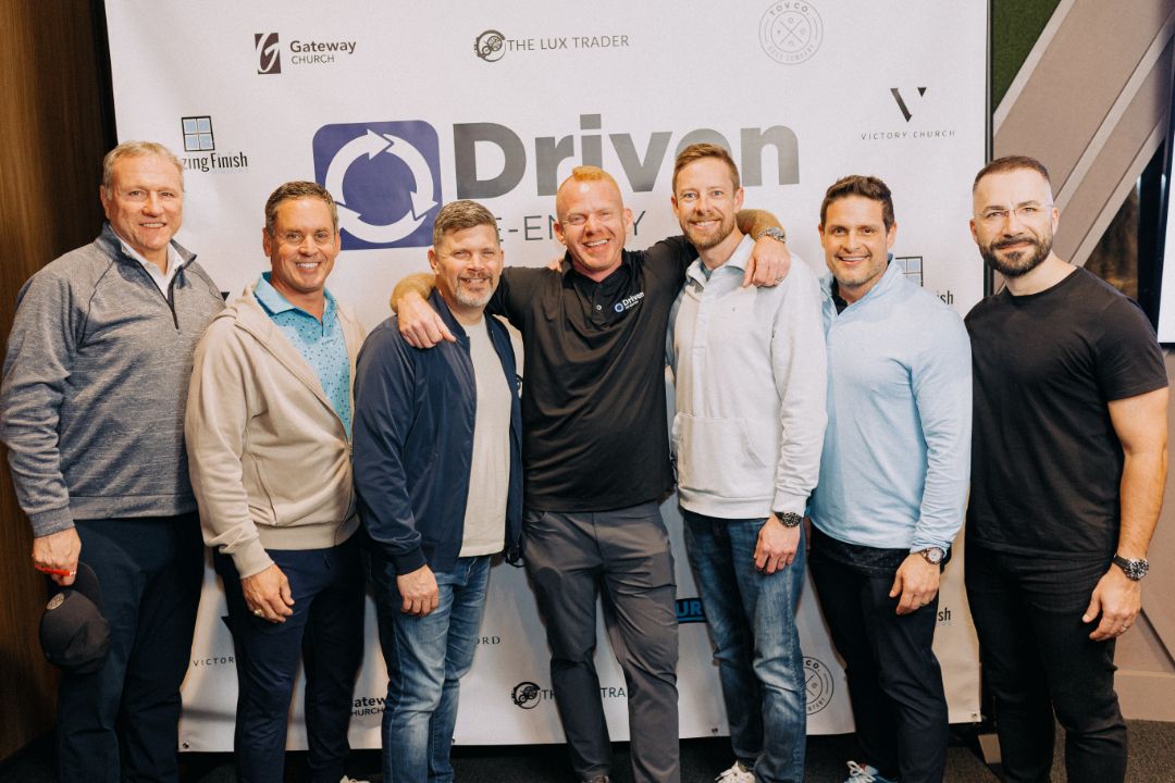 A group of men are posing for a picture in front of a sign that says driven.