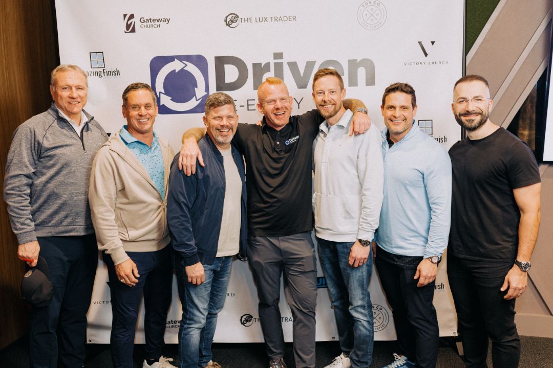 A group of men are posing for a picture in front of a sign that says driven.