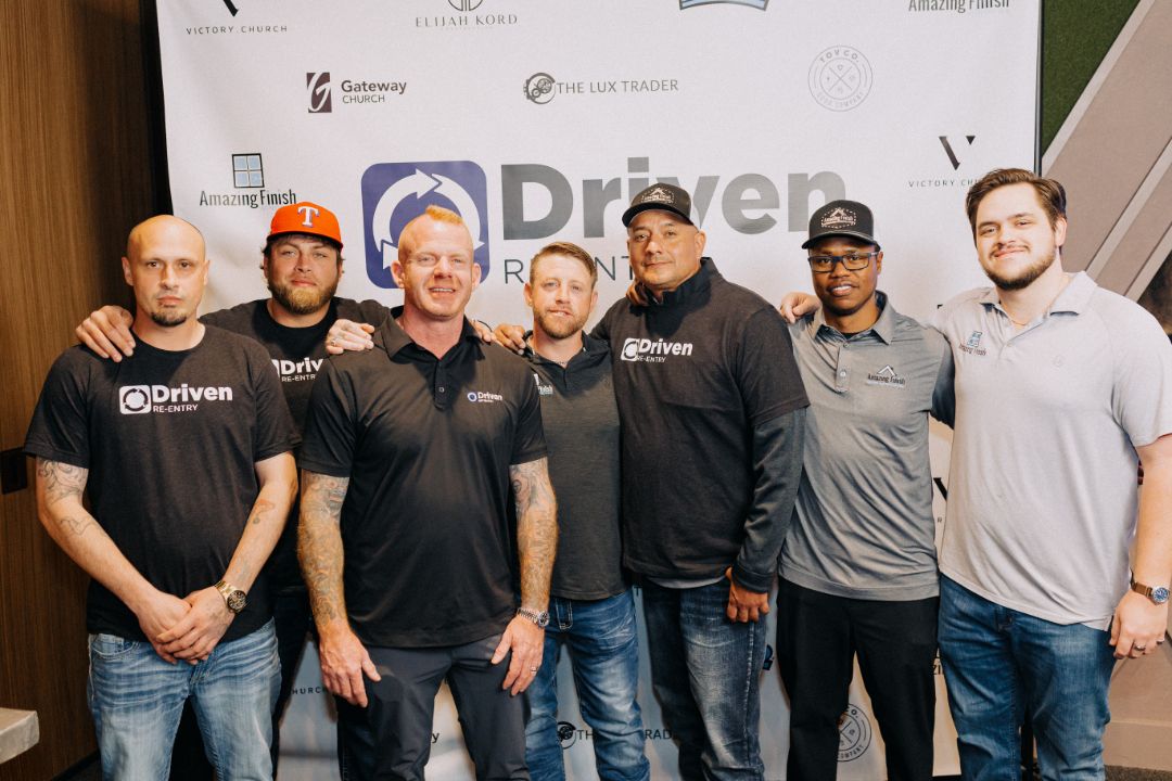 A group of men are posing for a picture in front of a sign that says driven.