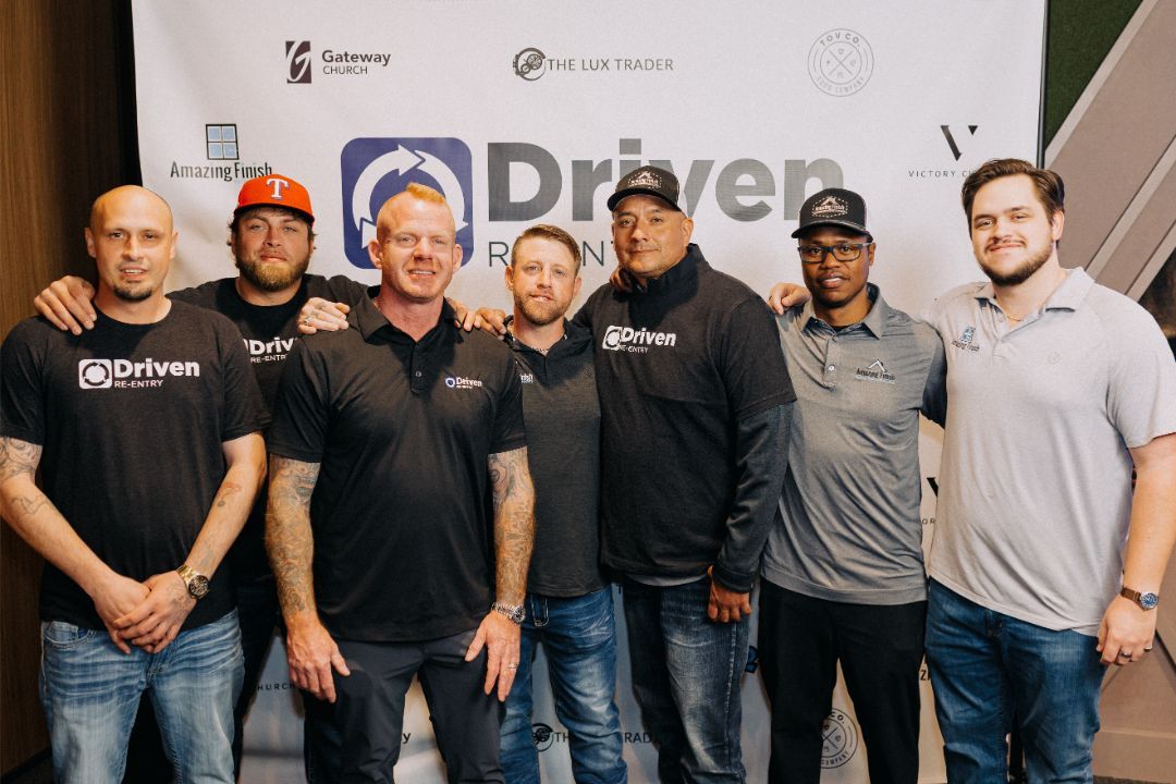 A group of men are posing for a picture in front of a sign that says driven.