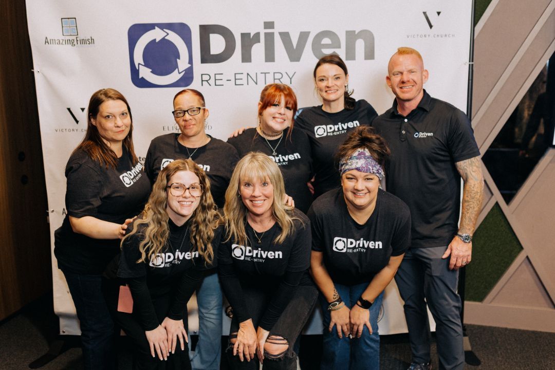 A group of people are posing for a picture in front of a sign that says driven.