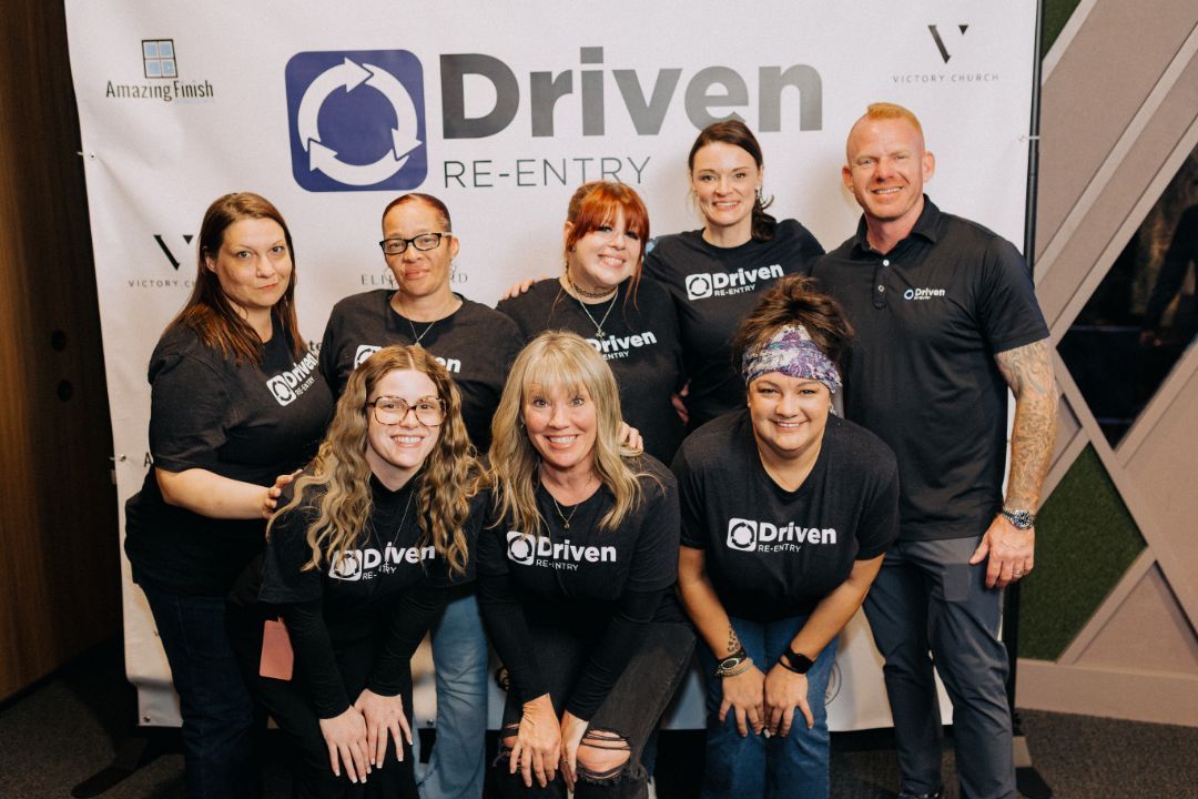 A group of people are posing for a picture in front of a sign that says driven.