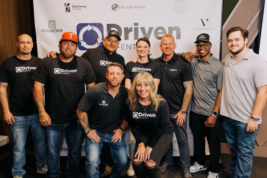 A group of people are posing for a picture in front of a sign that says driven.