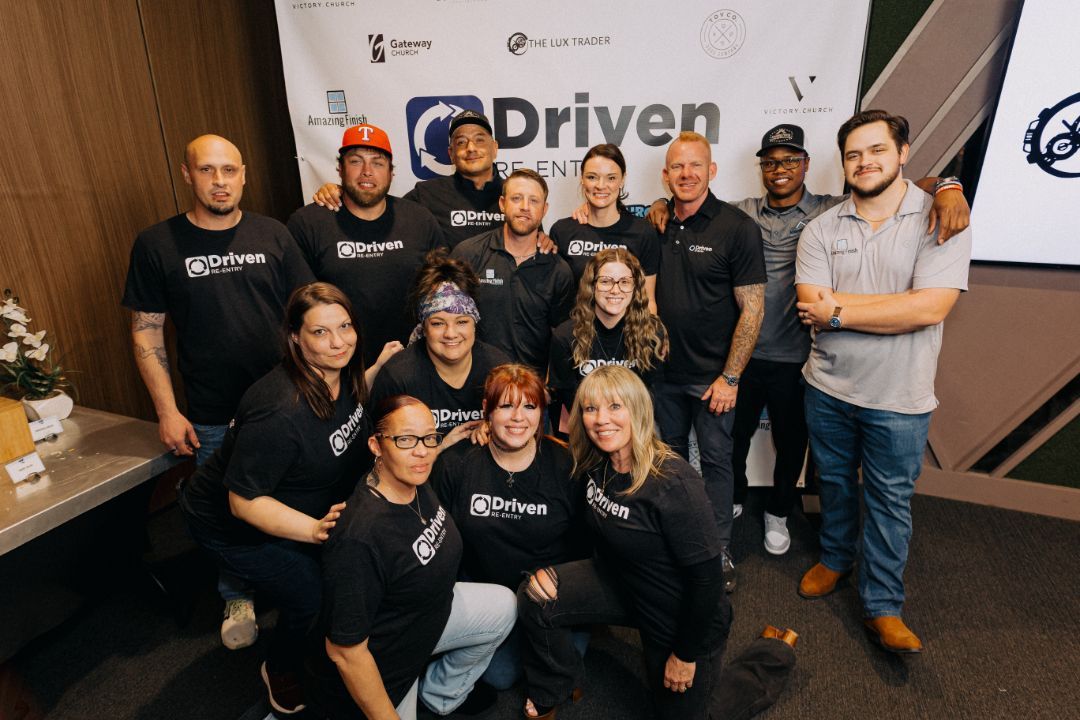 A group of people are posing for a picture in front of a sign that says driven.