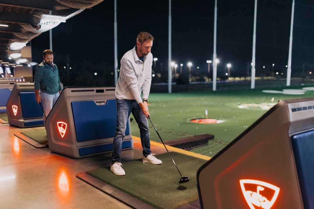 A man is swinging a golf club on a golf course at night.
