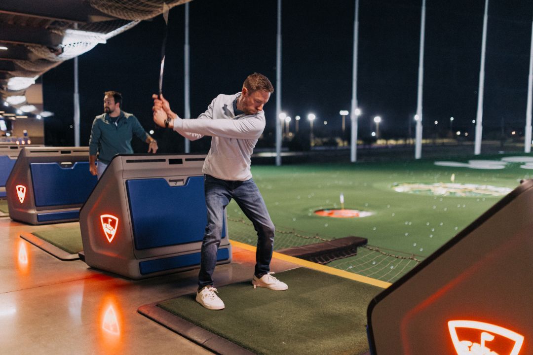 A man is swinging a golf club on a golf course at night.