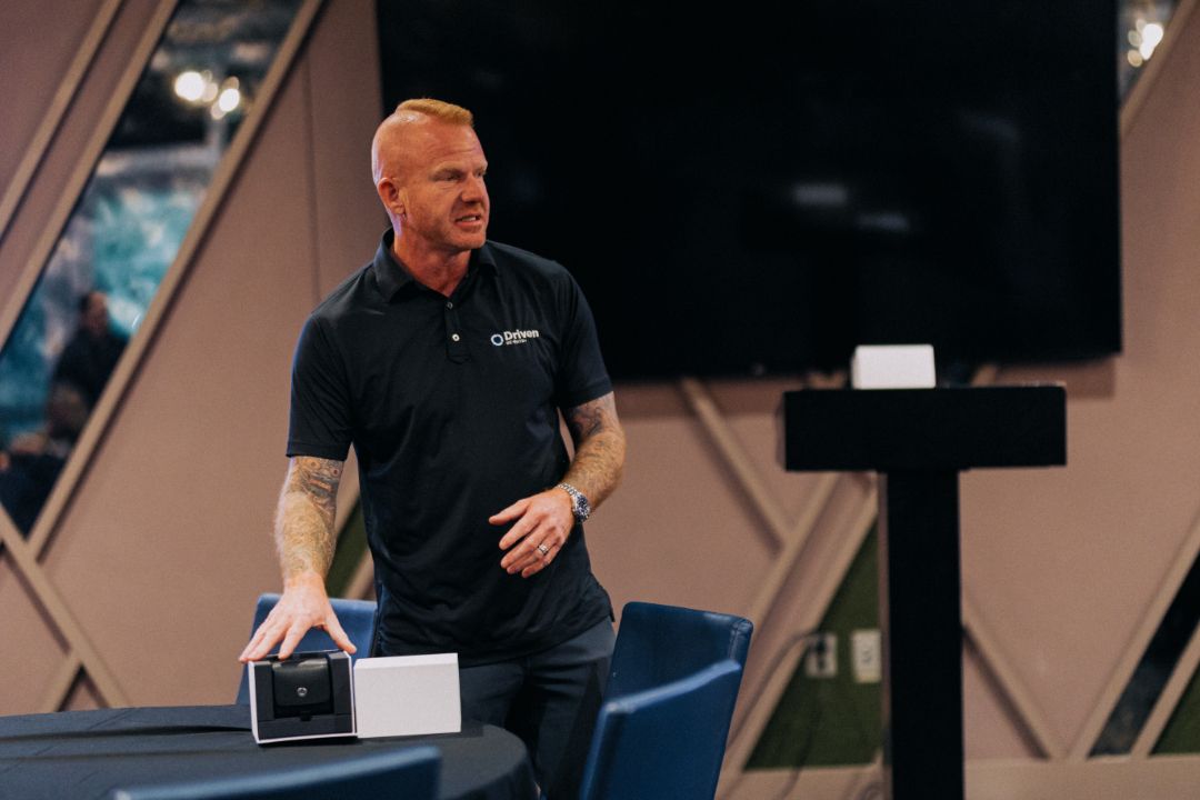 A man in a black shirt is standing in front of a table holding a box.