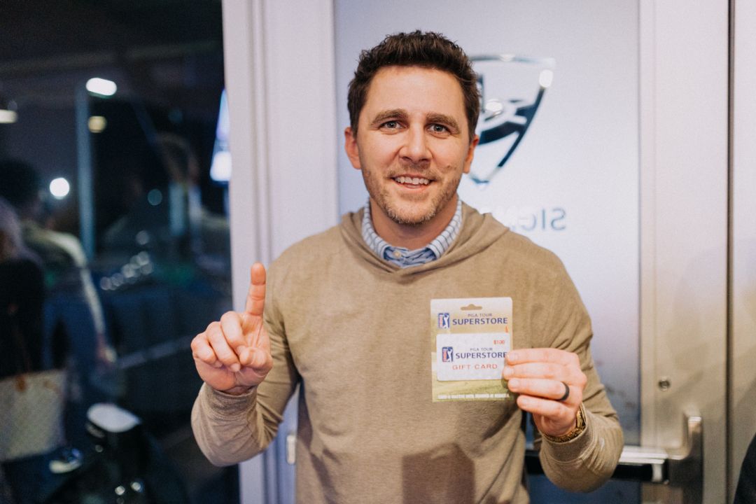 A man in a tan sweater is holding a name tag.