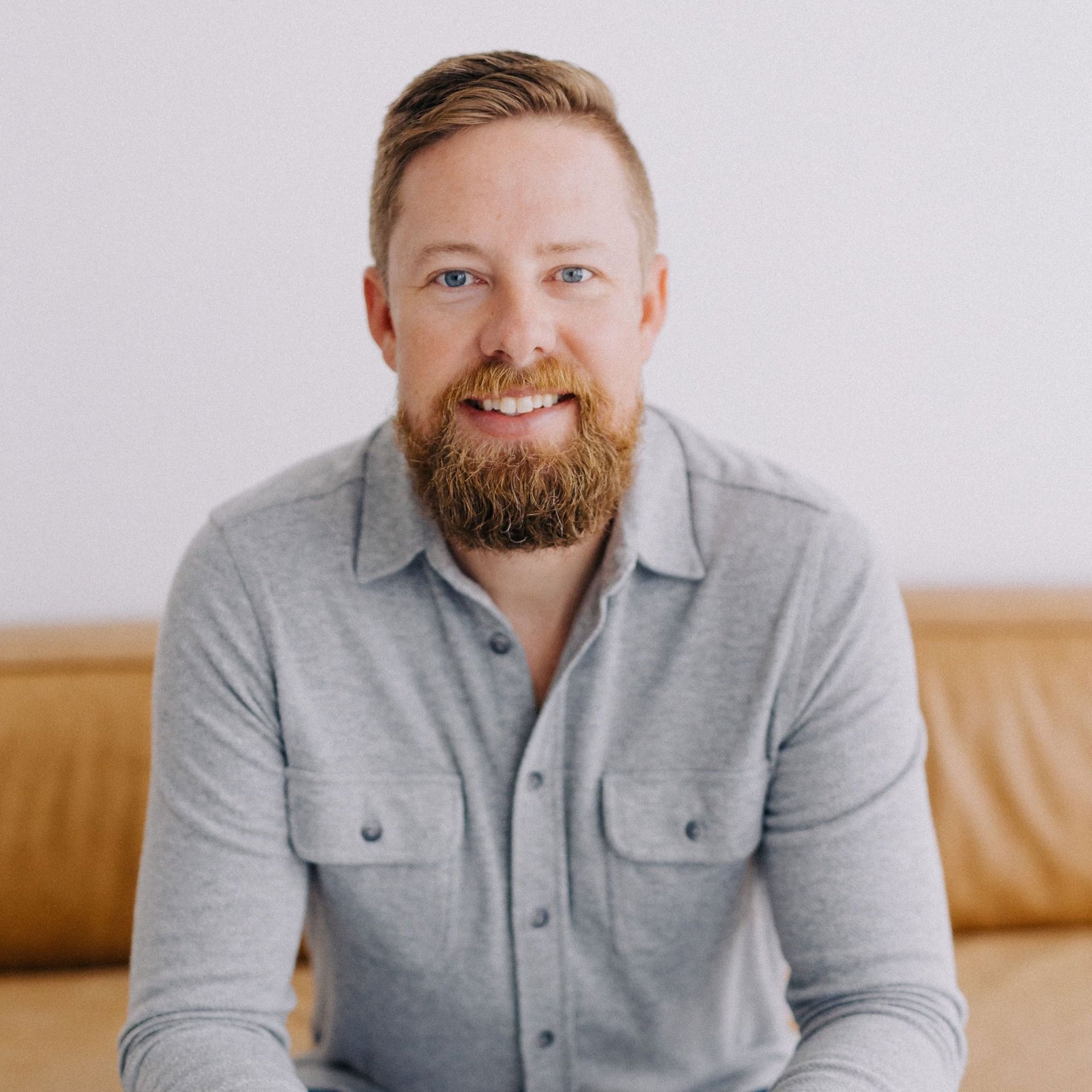 A man with a beard is sitting on a couch and smiling