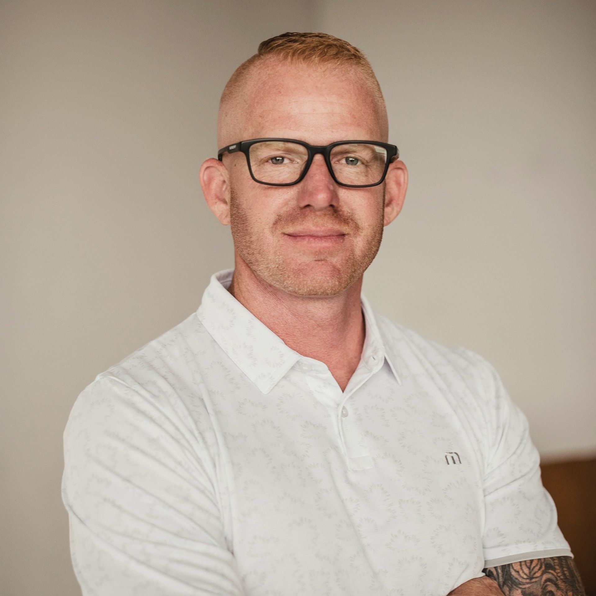 A man wearing glasses and a white shirt is standing with his arms crossed.