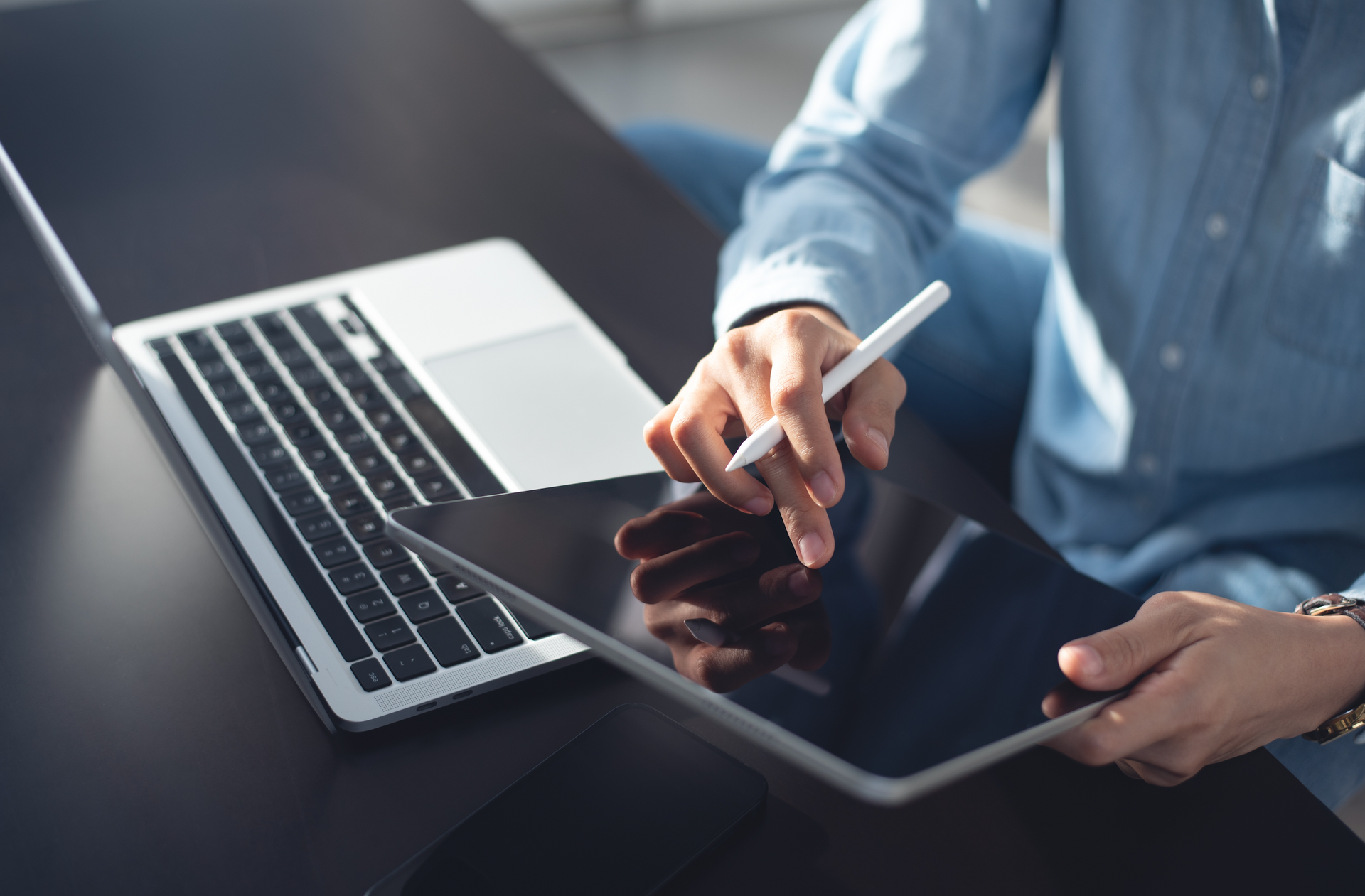 A man is sitting at a desk using a laptop and a tablet.