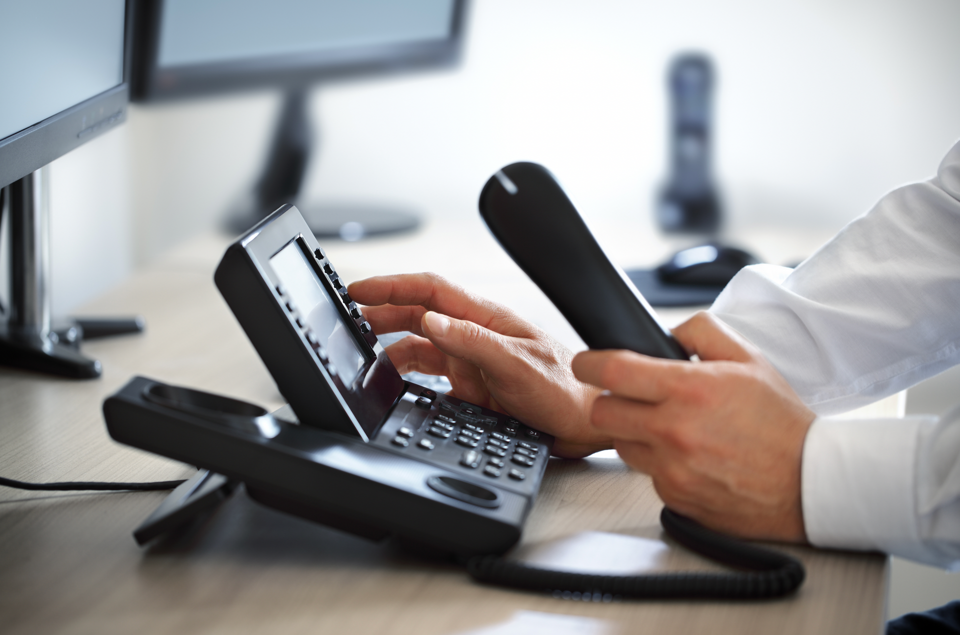 A man is typing on a telephone while sitting at a desk