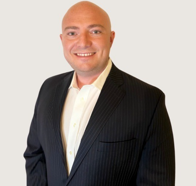 A man in a suit and white shirt smiles for the camera