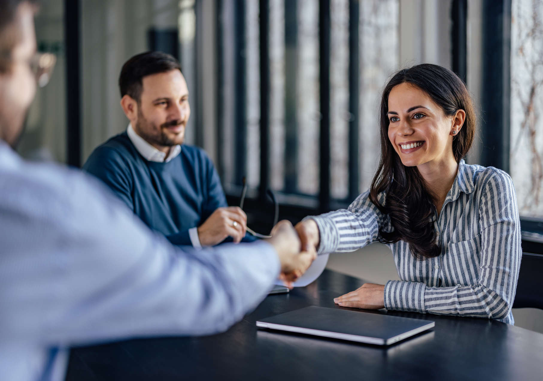 A man and a woman are shaking hands while sitting at a table.