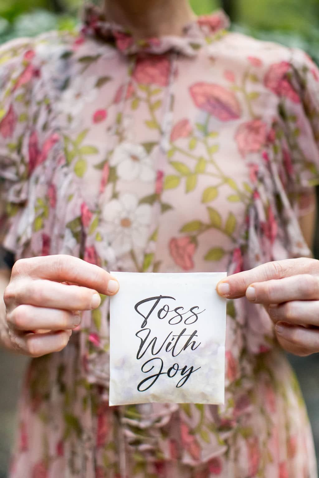 A woman in a floral dress is holding a piece of paper that says `` toss with joy ''.