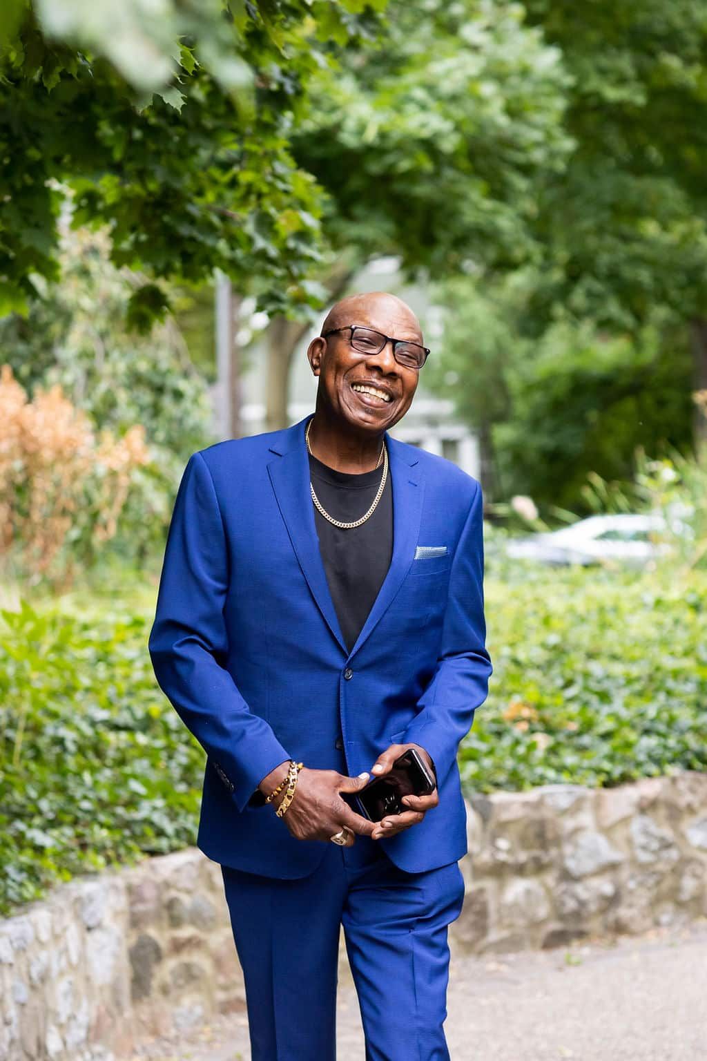 A man in a blue suit is walking down a sidewalk while holding a cell phone.