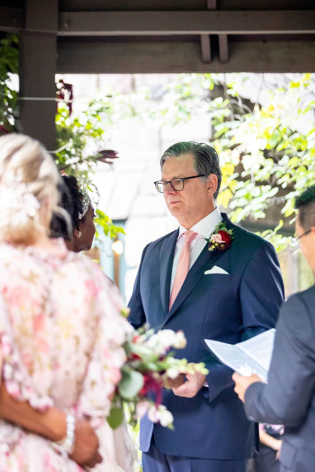 A man in a suit and tie is giving a wedding ceremony to a bride and groom.
