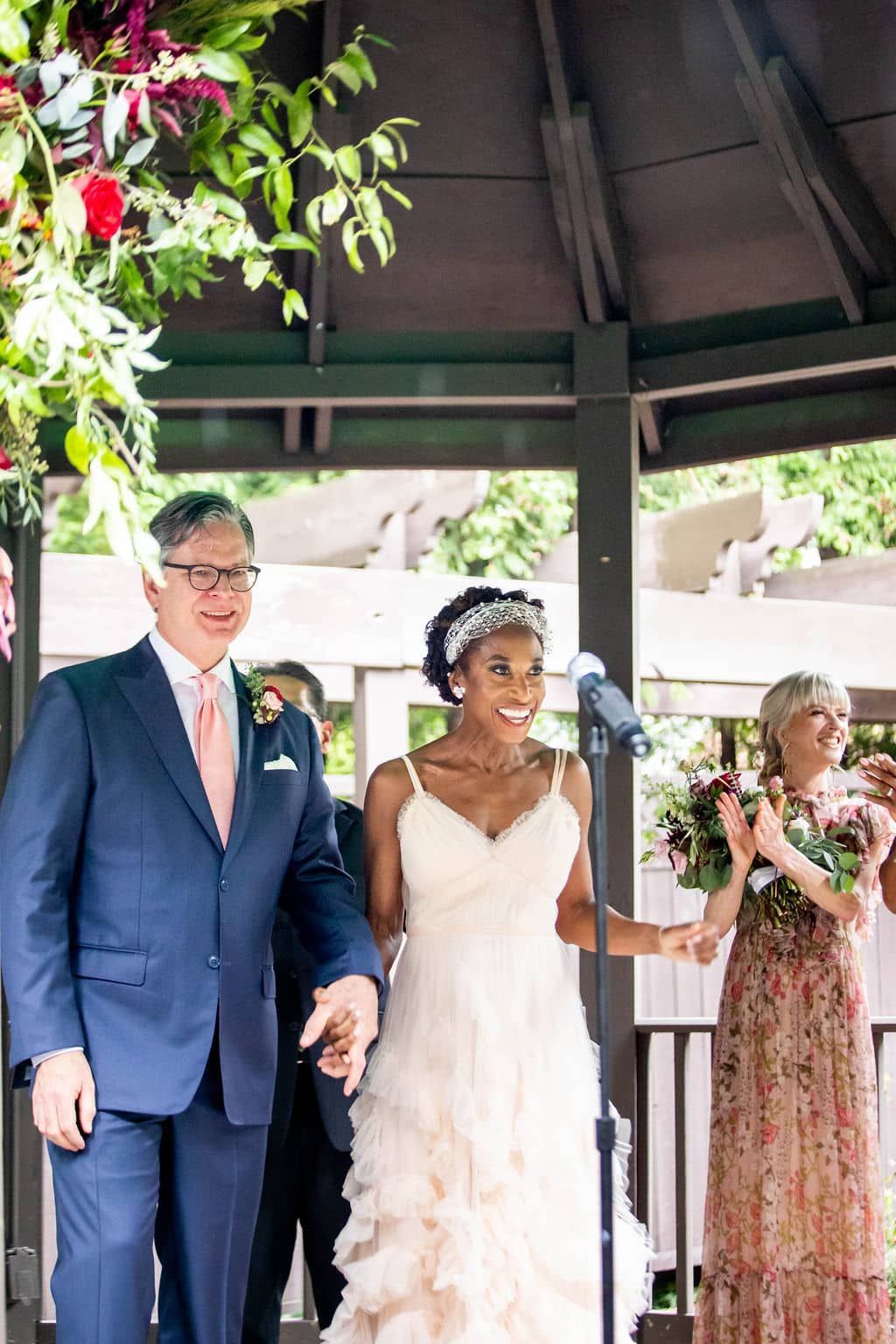 A bride and groom are walking down the aisle at their wedding under a gazebo.