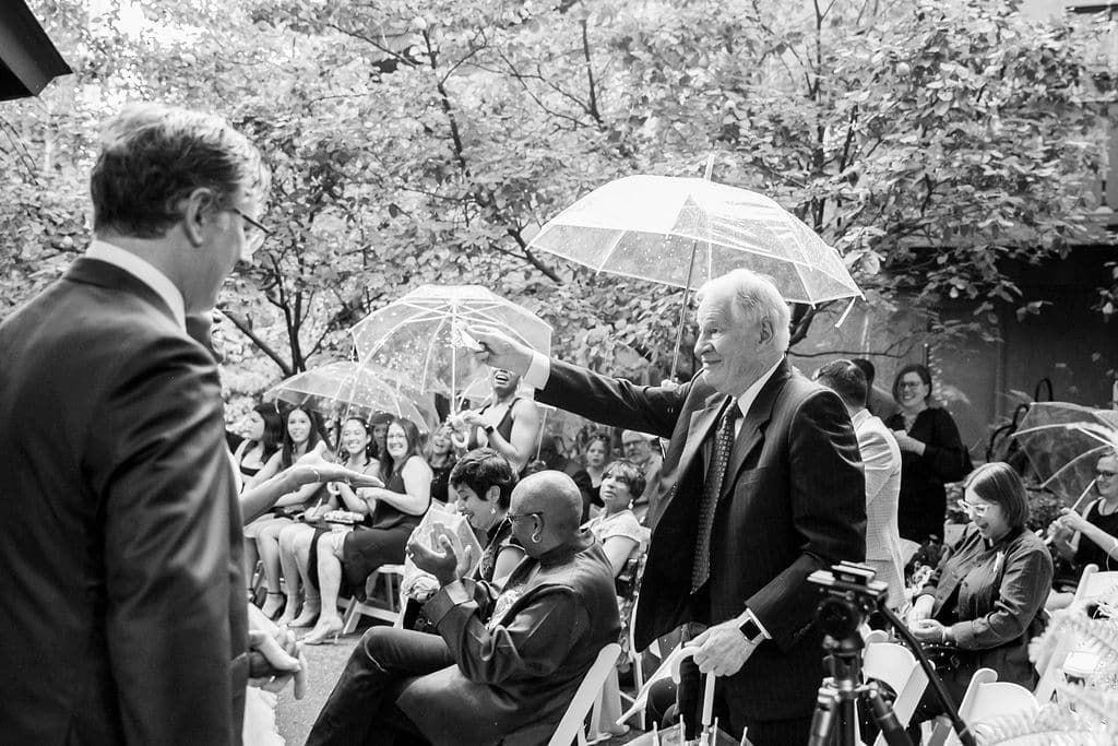 A man in a suit and tie is standing in front of a crowd of people holding umbrellas.