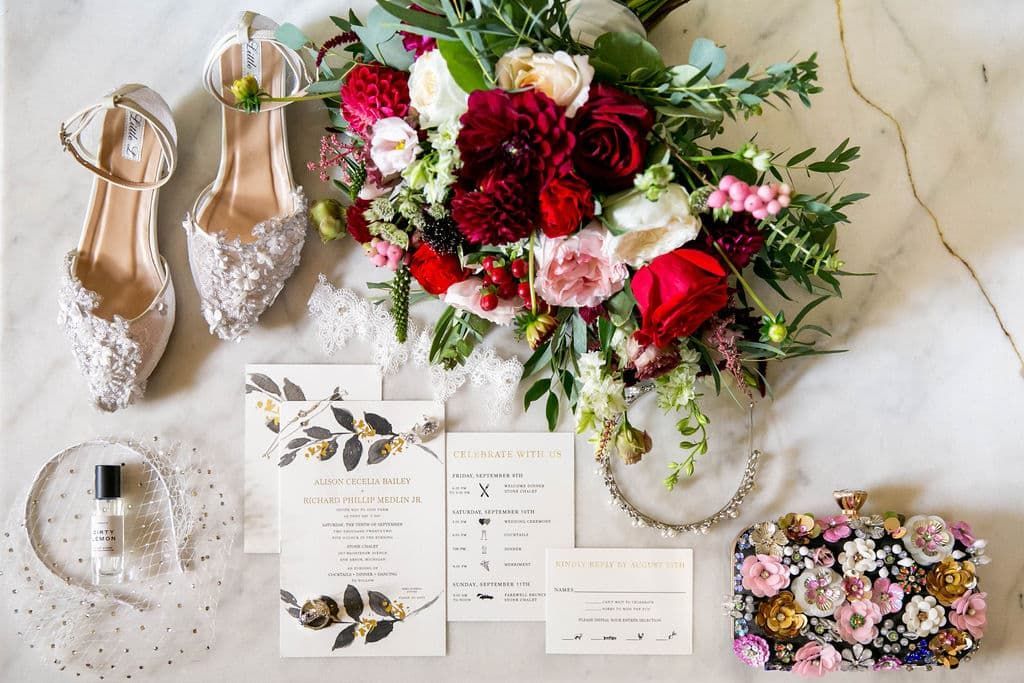 A bouquet of flowers , shoes , invitations , and a clutch are on a table.