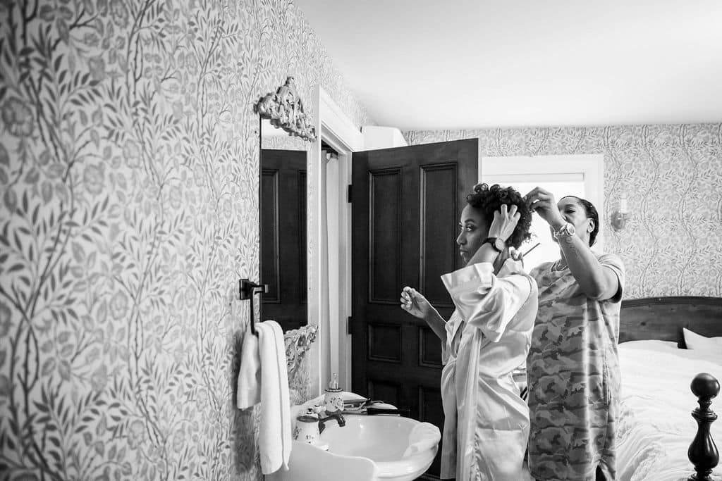 Two women are getting ready for a wedding in a bathroom.