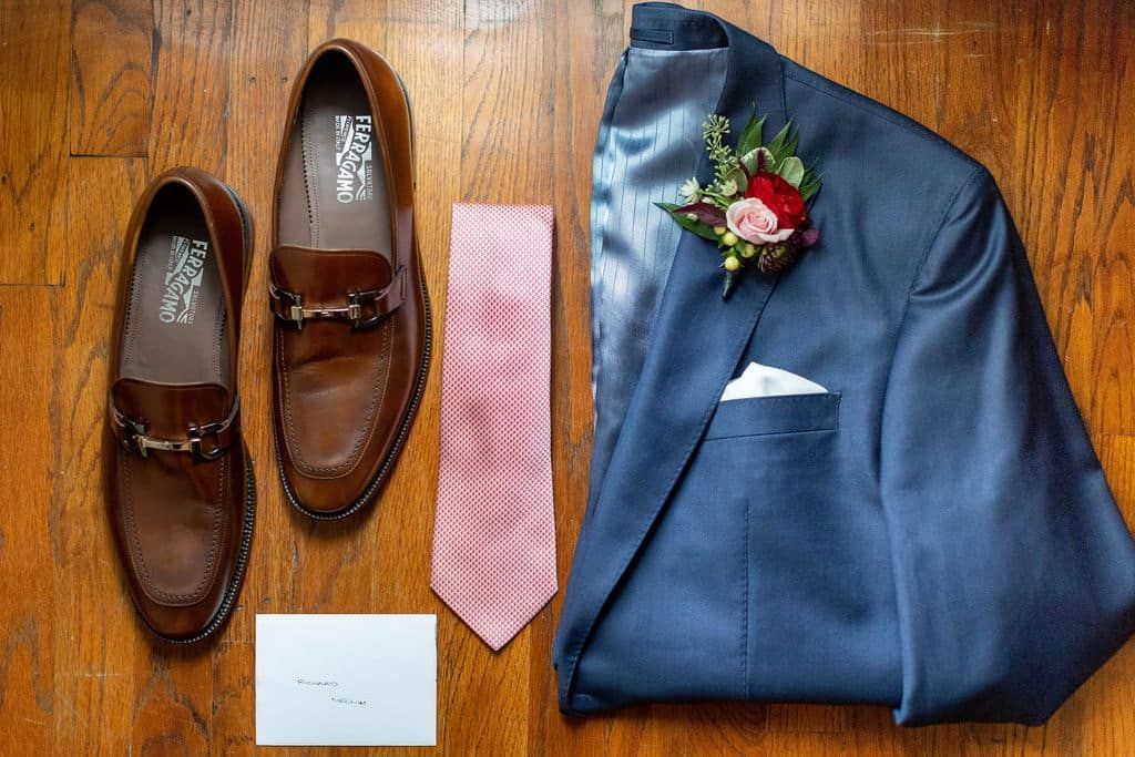 A pair of shoes , a suit , a tie and a pocket square are on a wooden floor.