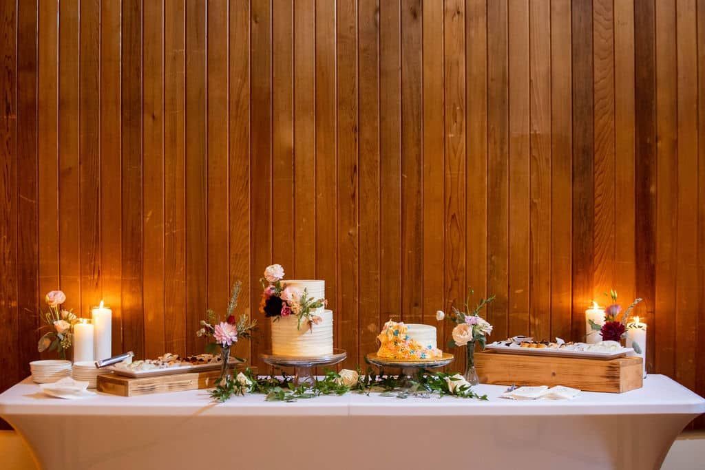A table with three cakes and candles on it in front of a wooden wall.