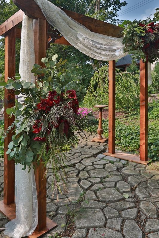 A wooden arch with flowers on it is sitting on top of a stone walkway.