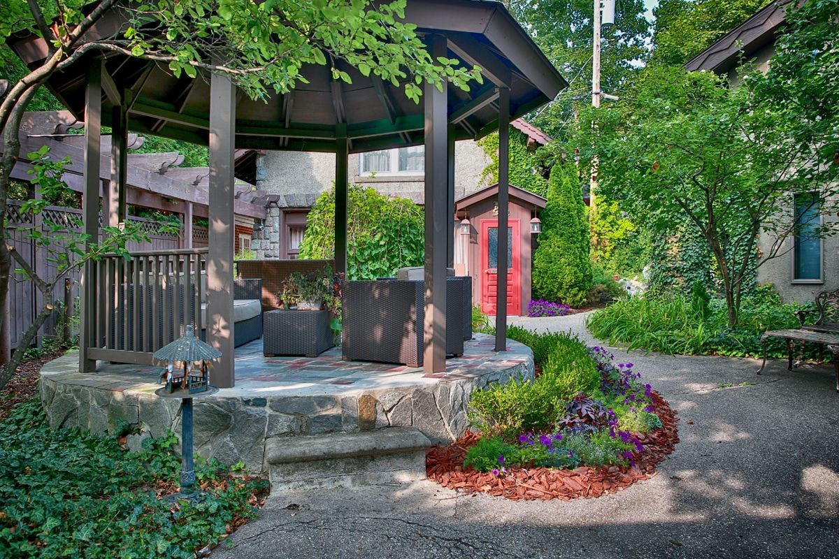 A gazebo in the middle of a garden with a red shed in the background.