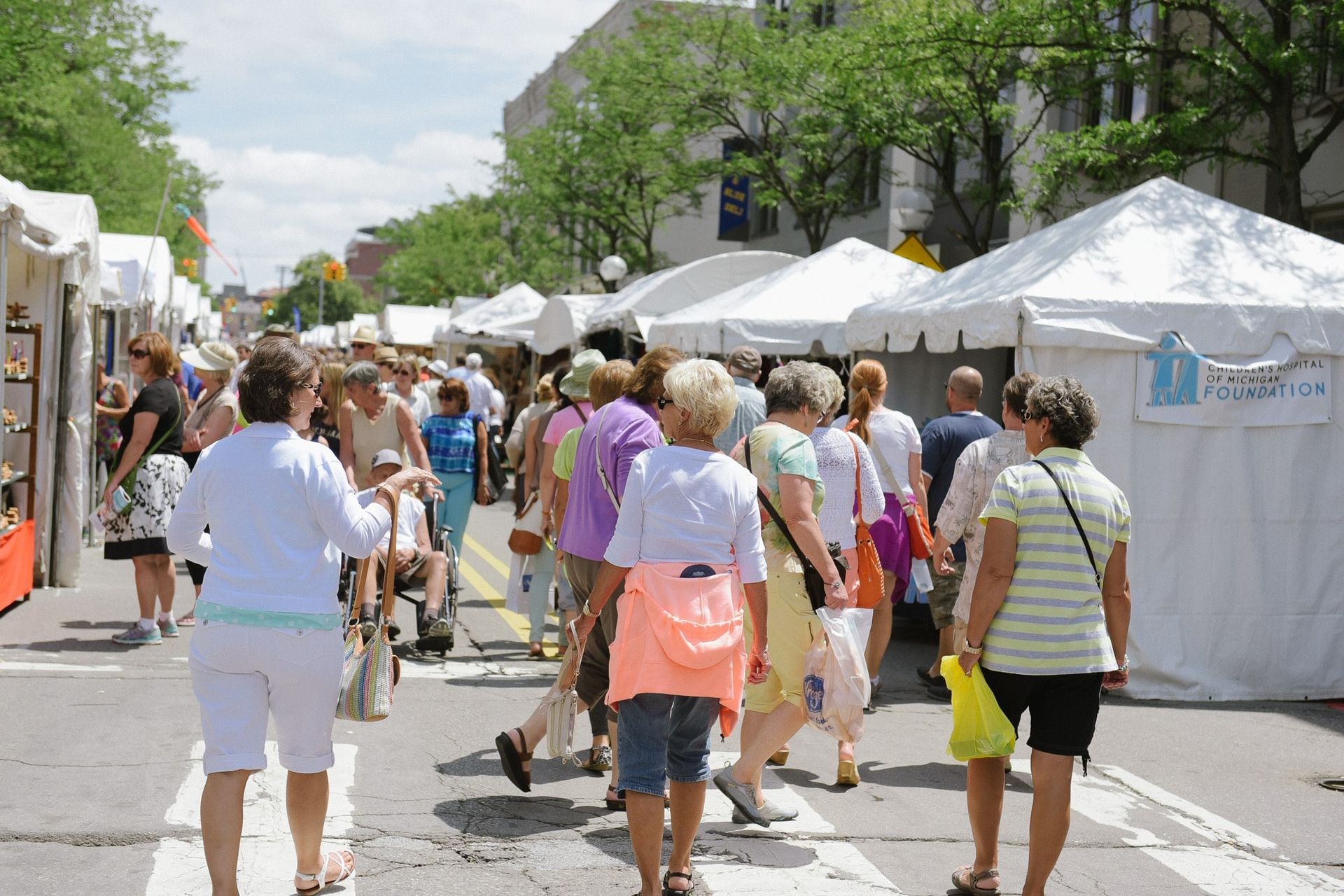 A group of people are walking down a street in front of tents.