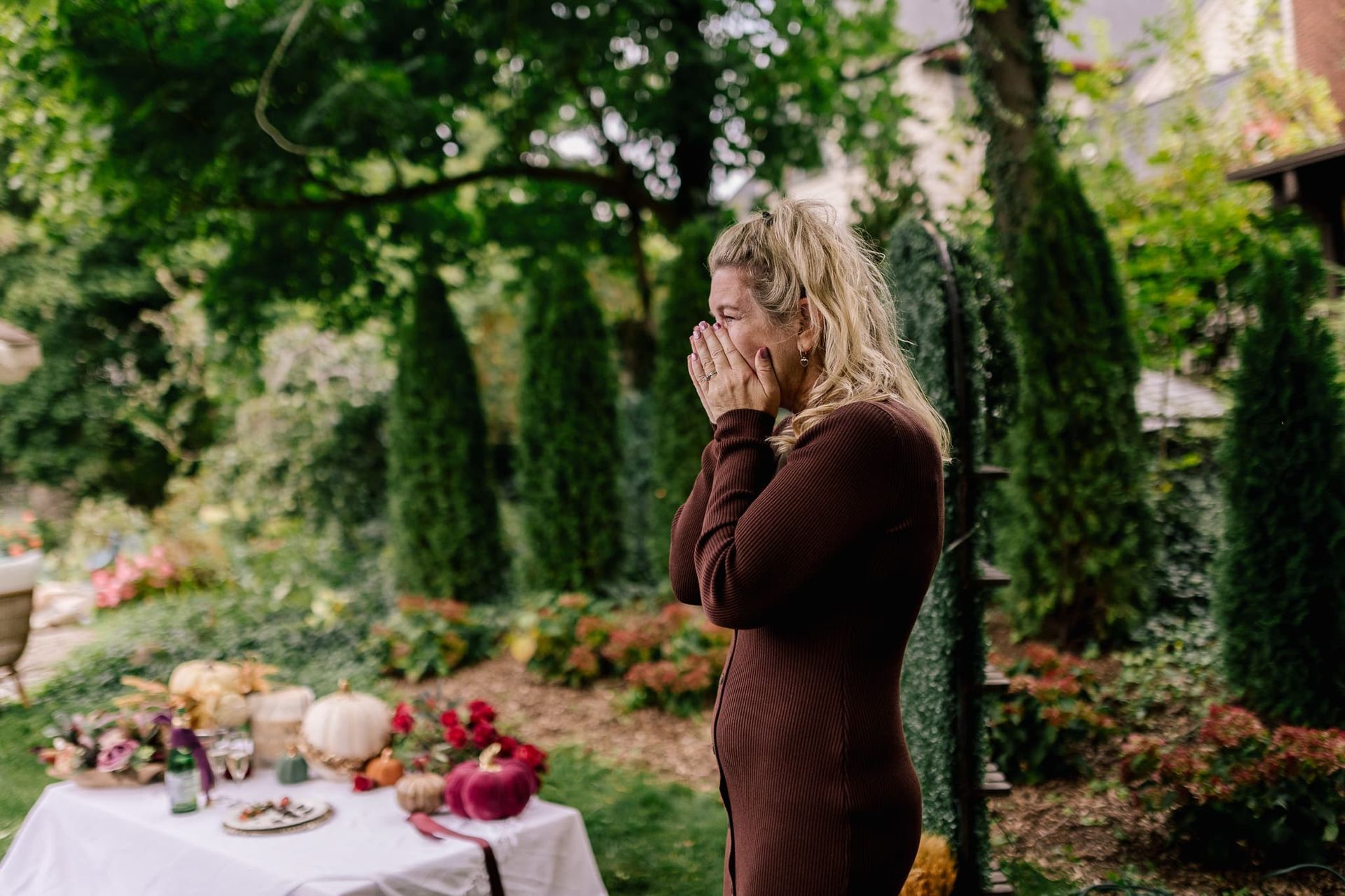 A woman is standing in front of a table with her hands on her face.