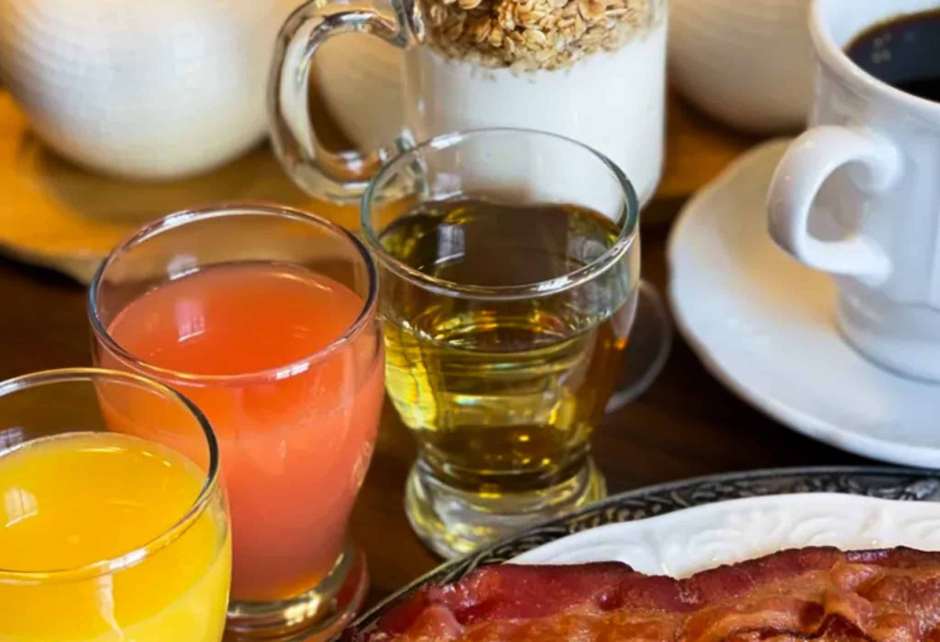 A table topped with a plate of bacon , juice , and coffee.