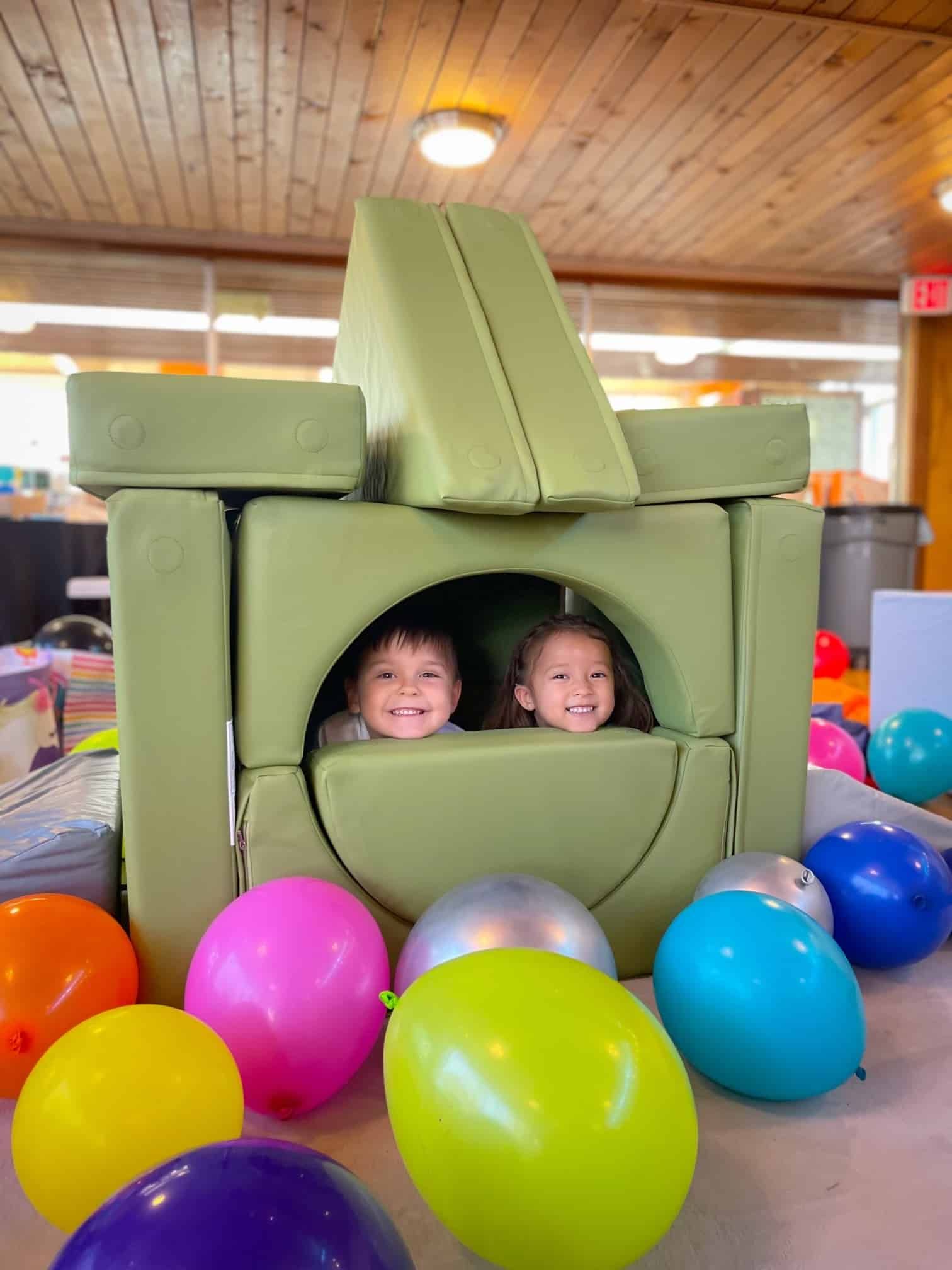 Two children are playing in a cube surrounded by balloons.