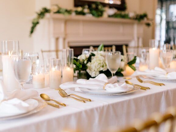 Elegant table setting with white linens, gold flatware, candles, and floral centerpieces.