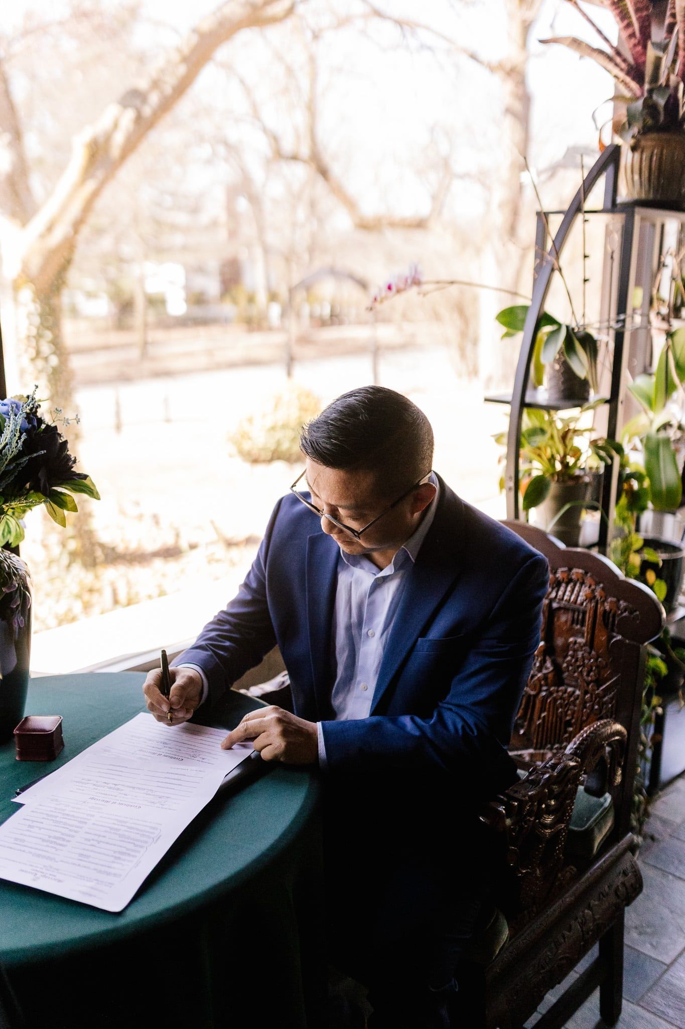 A man in a suit is sitting at a table writing on a piece of paper.