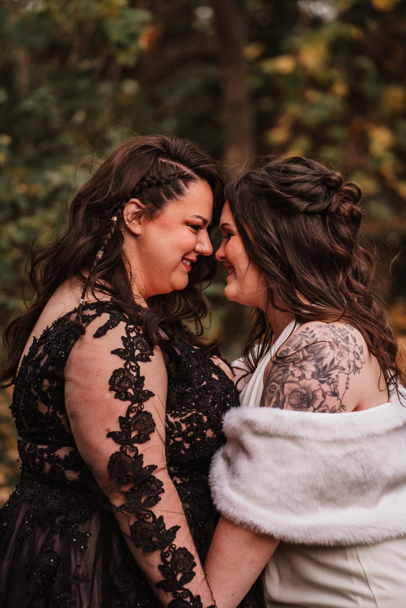 Two women in black dresses are holding hands and looking at each other.