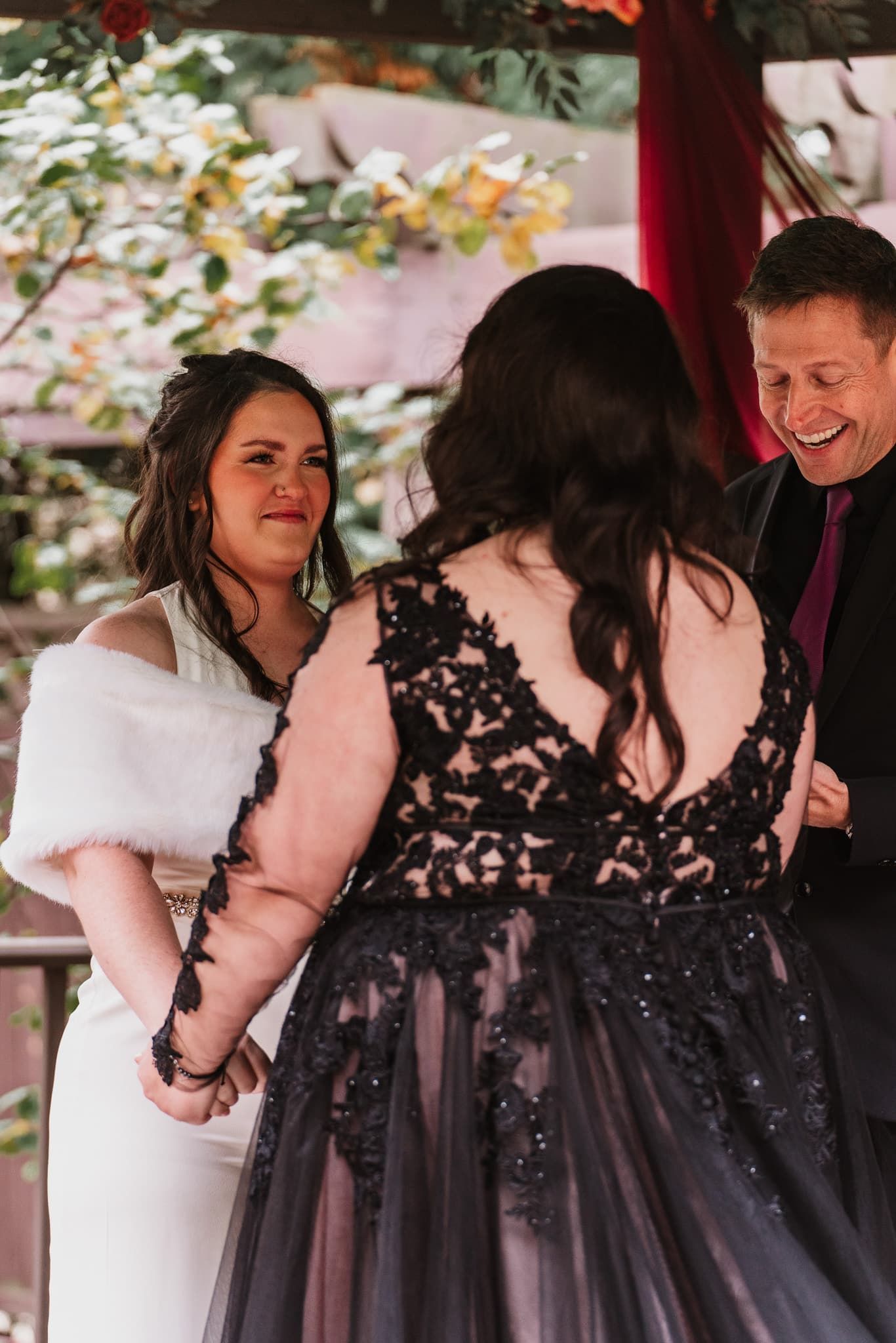 A woman in a black dress is holding hands with another woman in a white dress.