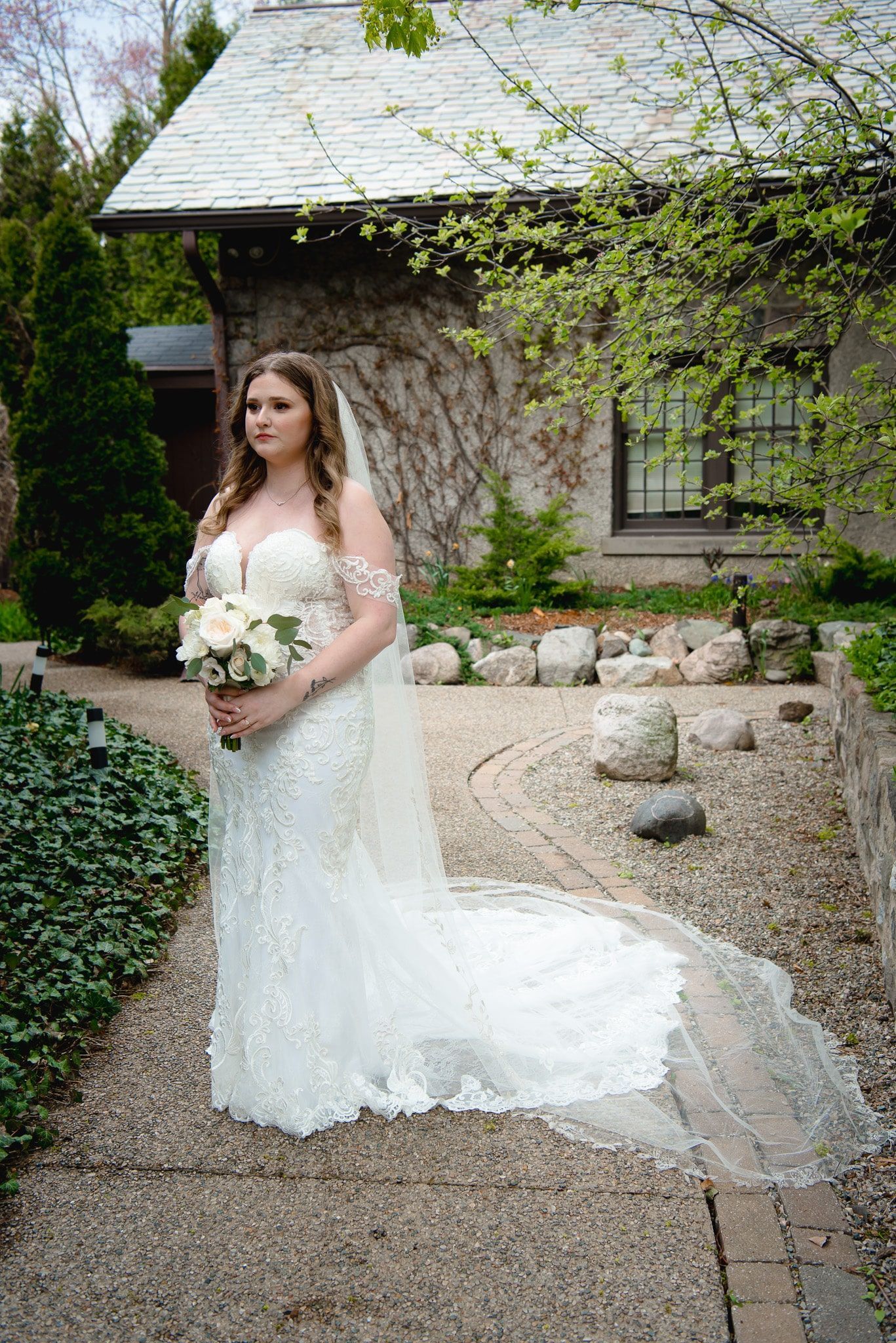A bride in a wedding dress is standing in front of a stone building holding a bouquet of flowers.