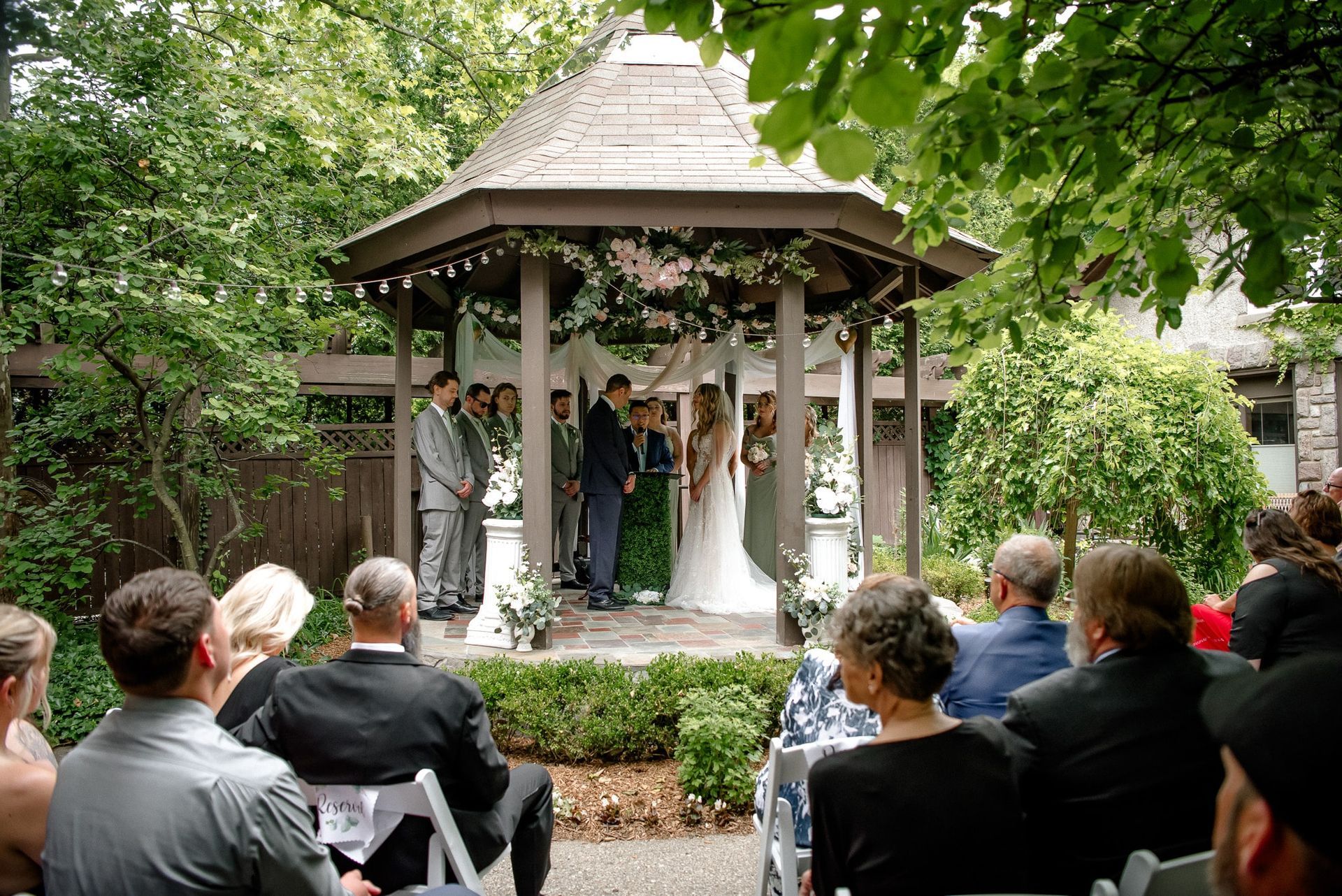 A group of people are sitting in chairs watching a wedding ceremony in a gazebo.