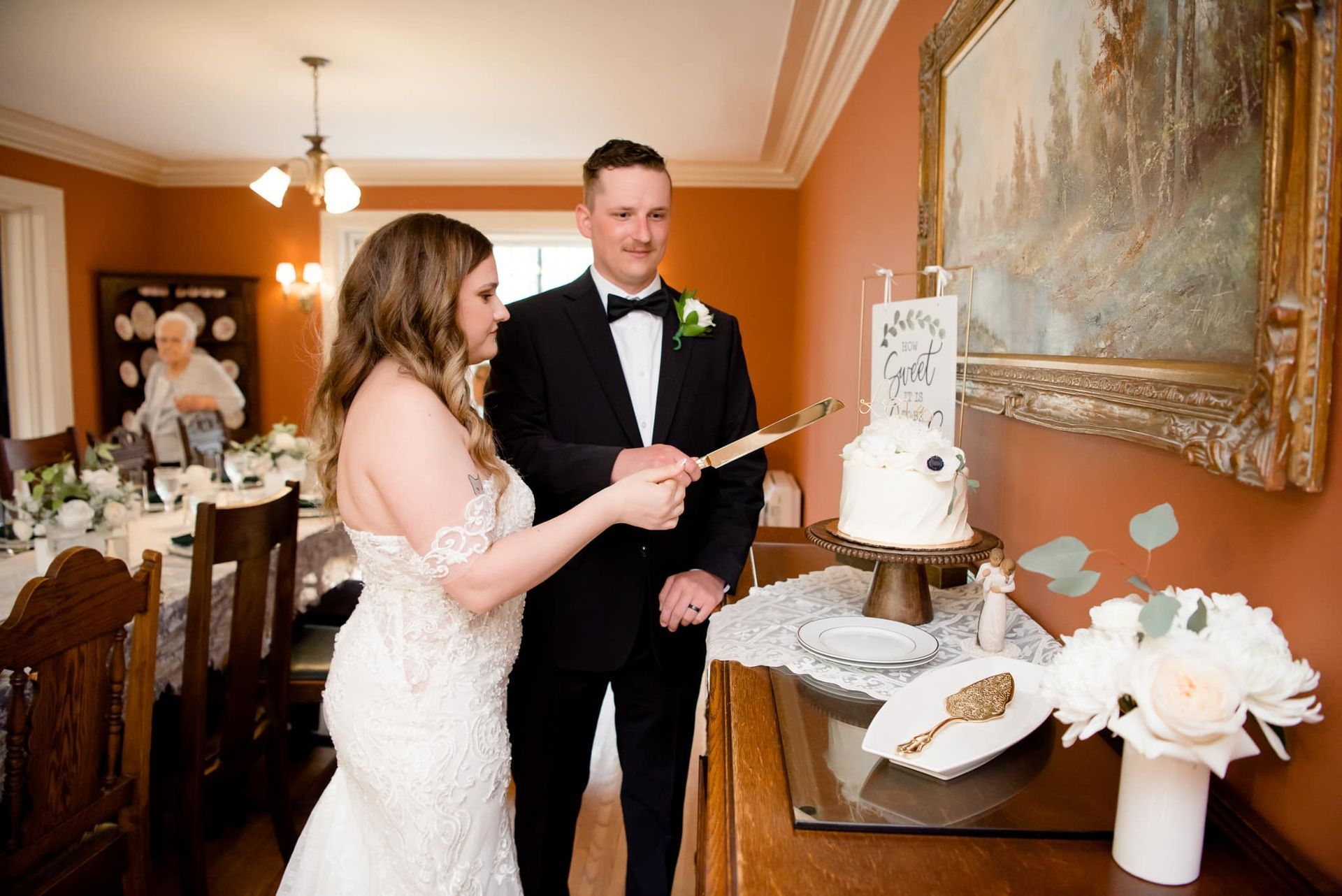 A bride and groom are cutting their wedding cake in a dining room.